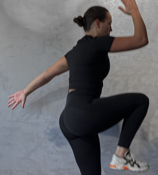 a woman in a black top is doing an athletic jump following an 8 week gym plan 